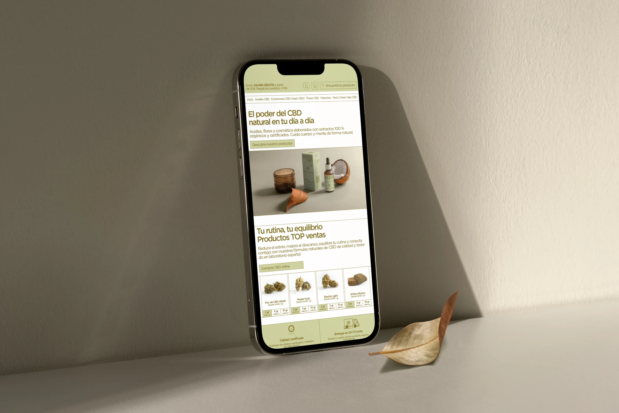 Smartphone apoyado en una pared junto a una hoja seca mostrando la tienda online de Green Nap Natural CBD, con la versión responsive de la web y el catálogo de productos desarrollada por DonDigital.