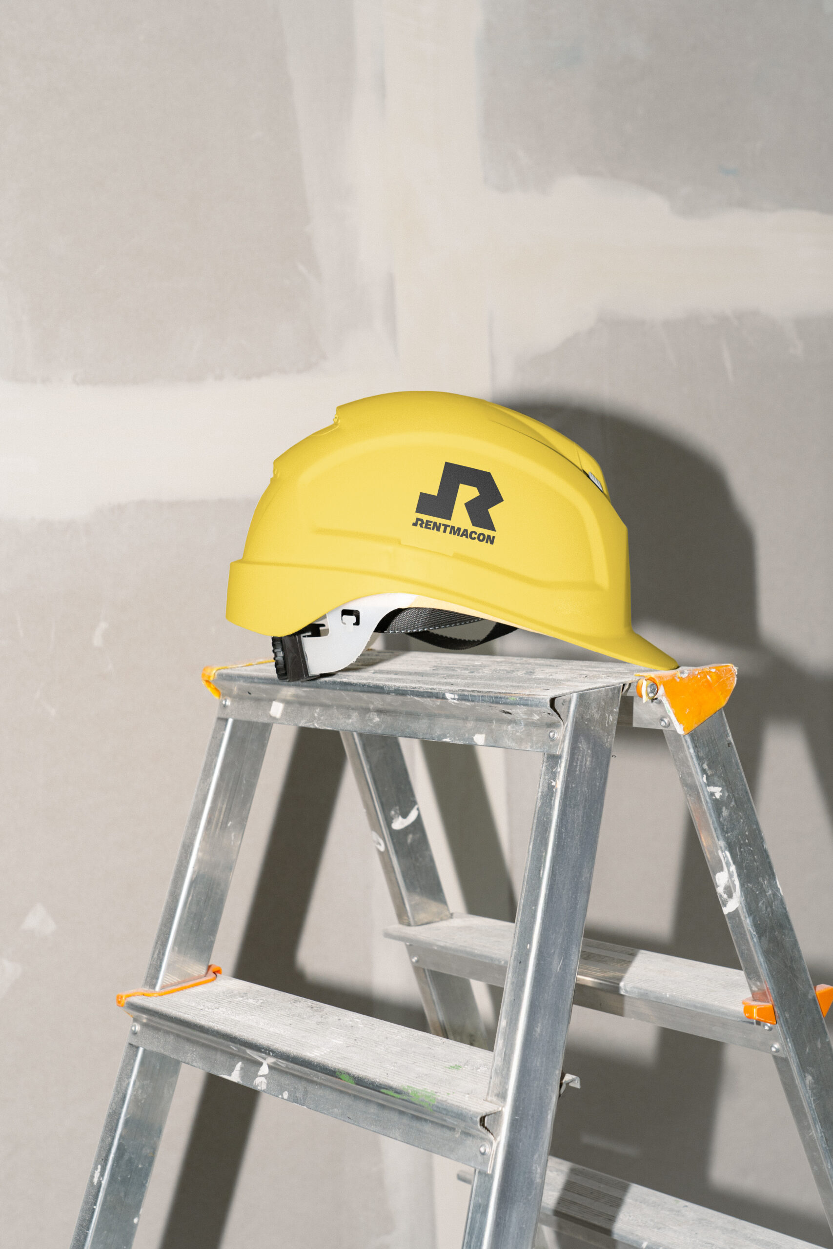 Casco de obra amarillo con el logotipo de Rentmacon sobre una escalera de aluminio en una reforma, fotografía de la marca realizada por DonDigital.