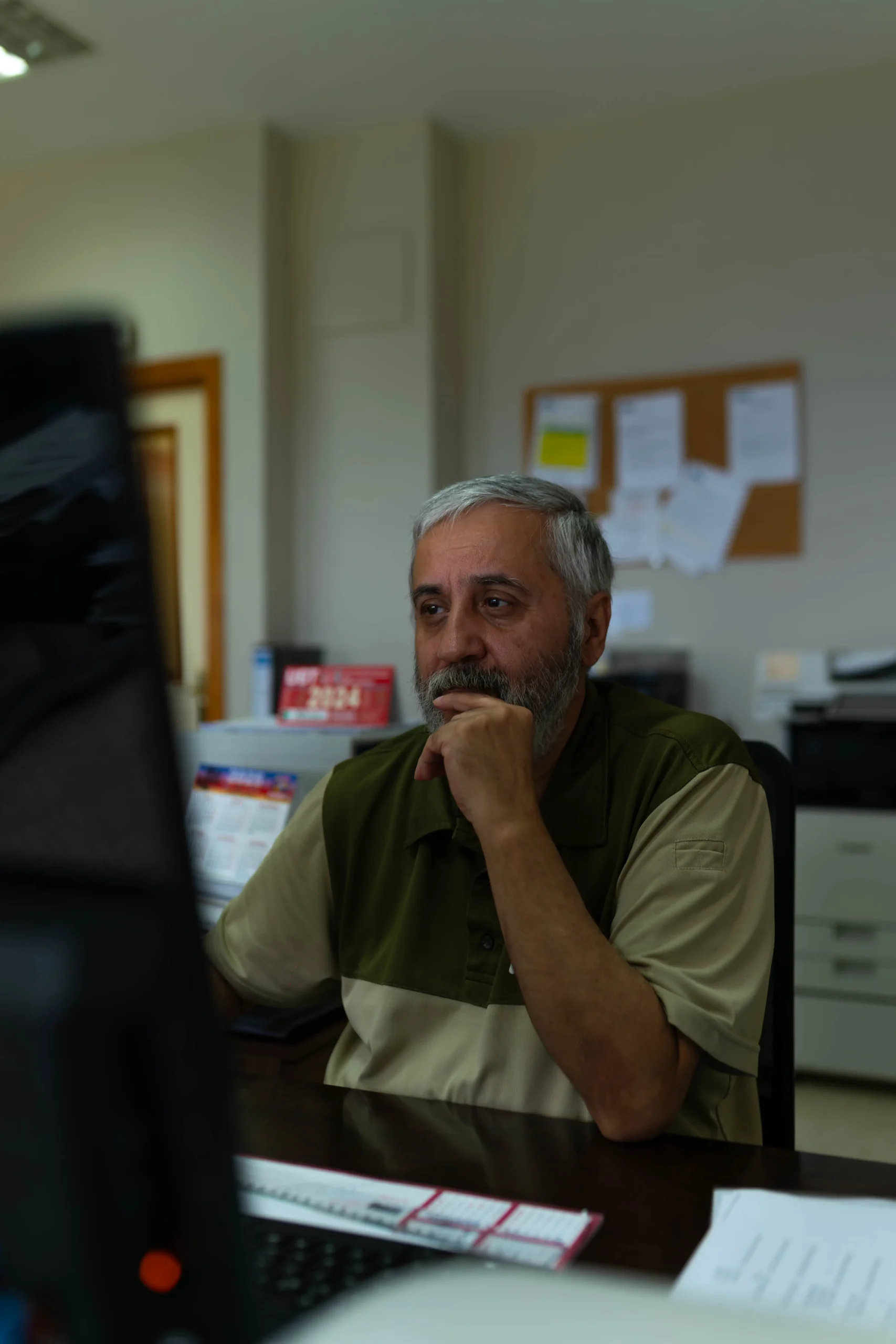 Trabajador con barba y polo corporativo de Obimasa reflexionando frente al ordenador en su puesto de la oficina de Obimasa, fotografía del personal realizada por DonDigital.